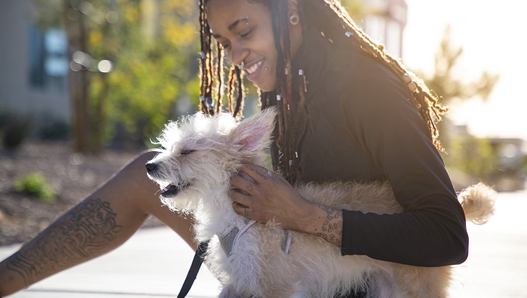 An androgynous African American person with there pet dog outdoors in a park.