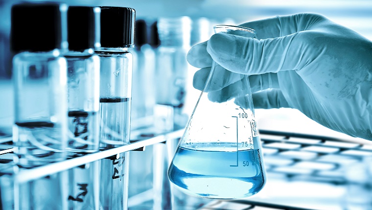 A scientists mixes liquid in a flask in a blue science lab.