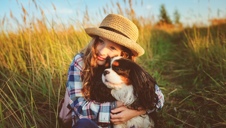 happy child girl enjoying summer vacations with her dog, walking and playing on sunny meadow. Traveling, exploring new places and rural living concept