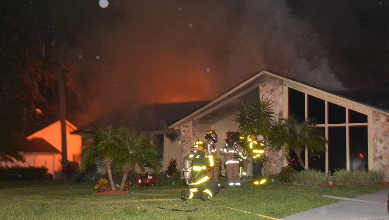 Firefighters stand outside the burning house.