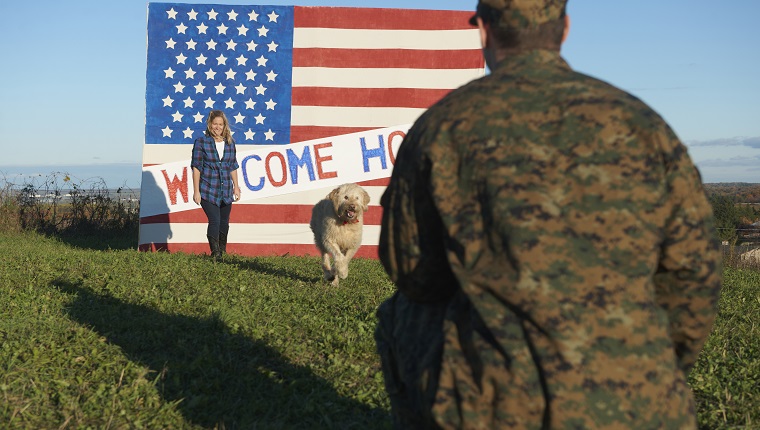 Returning Caucasian soldier greeting wife and dog