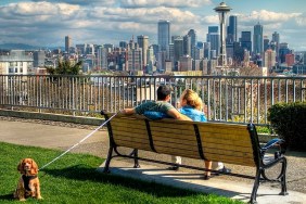 Man and woman sitting on park bench with dog on leash.