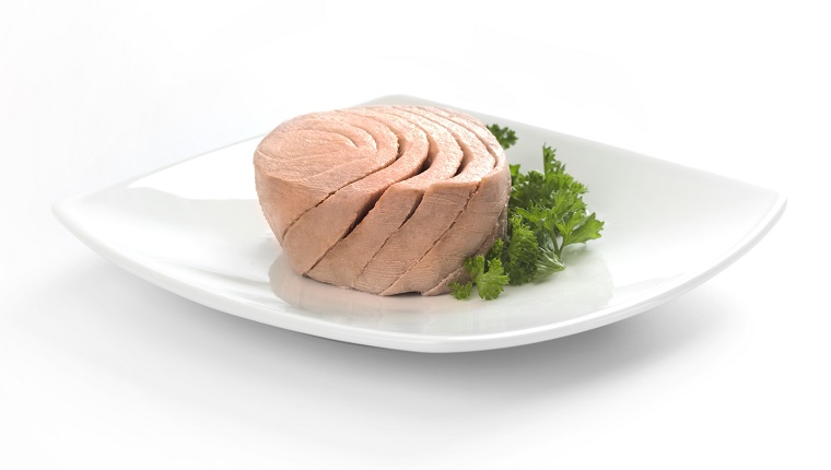 Canned tuna portion served on white dish with parsley.