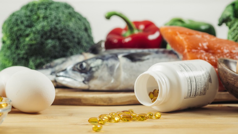 Supplement Bottle with Gel Capsules On a Wooden Table. Natural Food Sources of Vitamin D In Background.