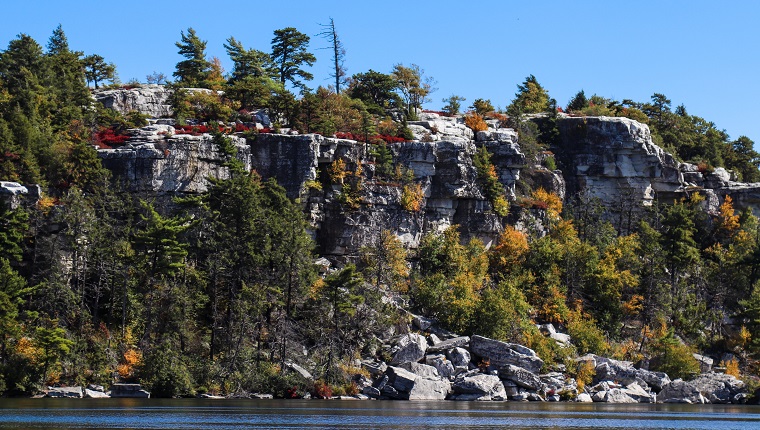 Photo with autumn colors on the trees with a beautiful lake, mountains, and sky in a New York state park - view of cliffs from across the lake