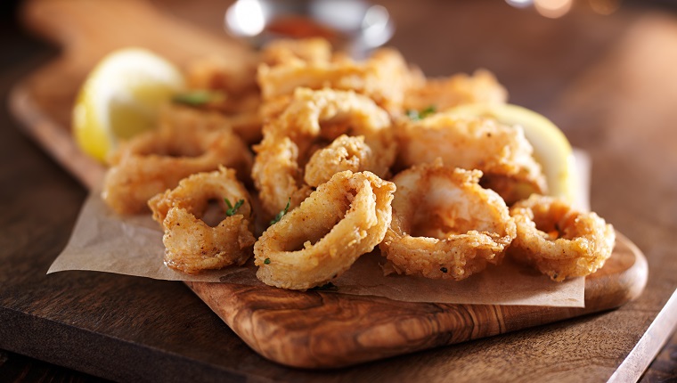 fried calimari rings on wooden tray with dipping sauce shot with selective focus