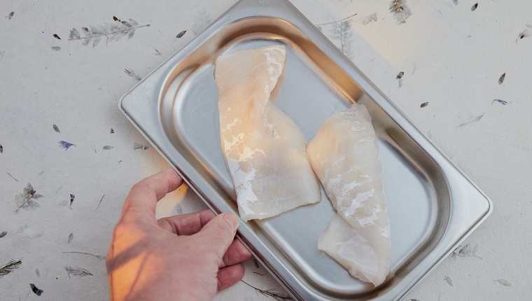 Cod fillets in stainless steel kitchen tray. Decorative surface. Amber light effect.