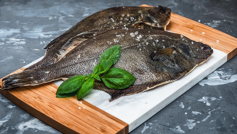 Raw fish flounder with salt and basil on a kitchen board close-up