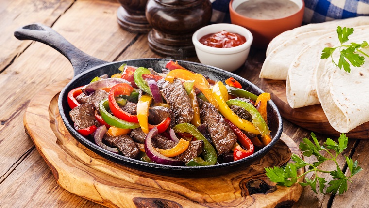 Beef Fajitas with colorful bell peppers in pan and tortilla bread and sauces