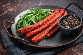 Dry smoked Kabanos or cabanossi traditional Polish thin sausages on a steel tray. Dark background. Top view.