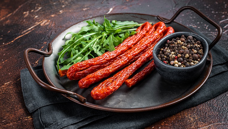 Dry smoked Kabanos or cabanossi traditional Polish thin sausages on a steel tray. Dark background. Top view.