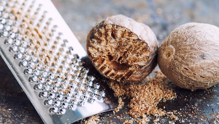 Nutmeg grater macro view. Kitchen still life photo close-up muscat nut powder. Shallow depth of field, vintage brown rusty background. Selective focus.