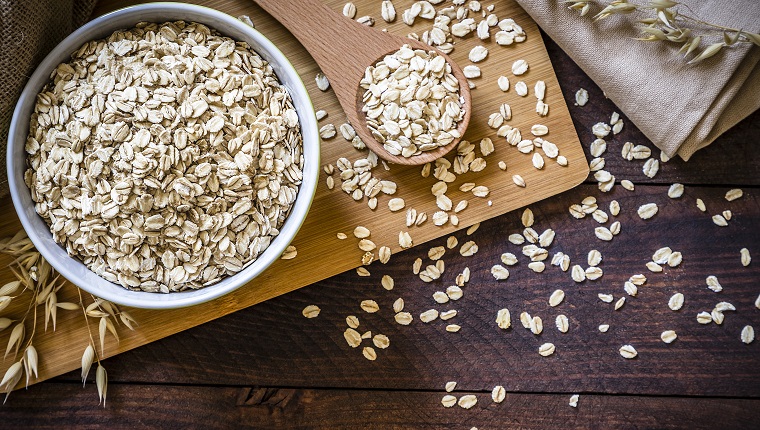 Top view of a bowl filled with uncooked oat flakes with a wooden spoon on wooden table. There is a useful copy space in the lower right corner