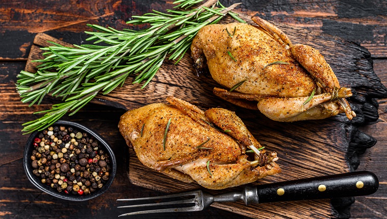 Homemade baked quail on a cutting board. Dark Wooden background. Top view.