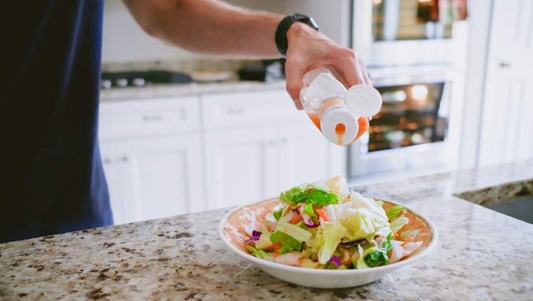 Close-up of unrecognizable white male pouring salad dressing onto salad