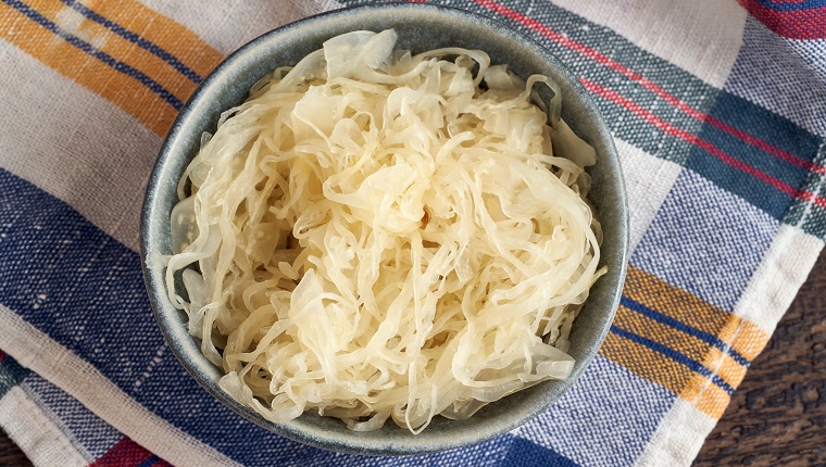 Fermented cabbage in a bowl on a colorful dish towel, top view