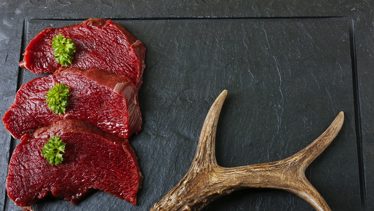 Raw steak meat from roe deer on the bridlic chopping board. Roe deer antler as a decoration. Copy space for text.