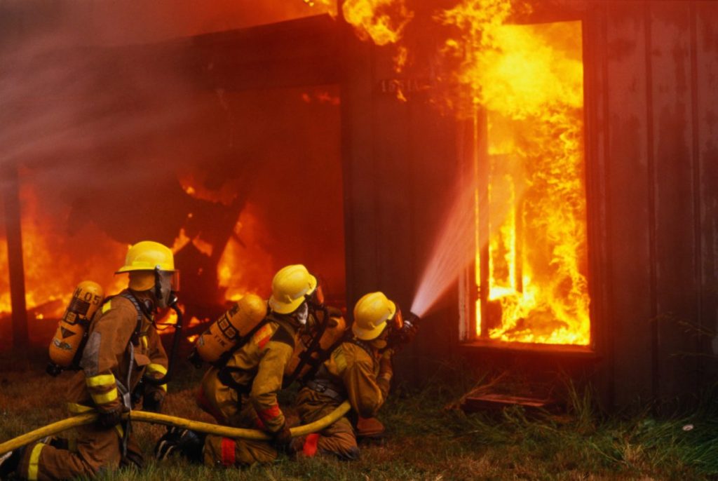 Three firefighters holding a water hose as they extinguish a burning house, like the ammunition-fueled house fire in Sylmar.