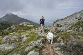 Man hikes with dog on Avery Peak above Flagstaff Lake along the Appalachian Trail in Maine's Bigelow Mountains