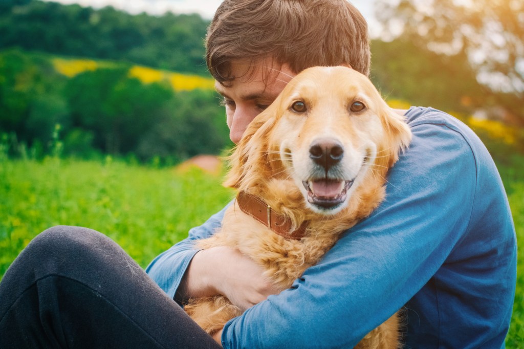 Man hugging his Golden Retriever outdoors.