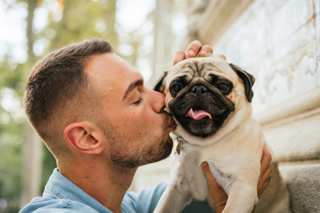 Young man kissing Pug outdoors.