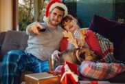 Young couple at home with their pet dog, watching Christmas movies on the television.