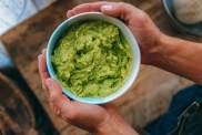 Photograph of a man's hands holding a bowl of guacamole, which is not safe for dogs to eat.