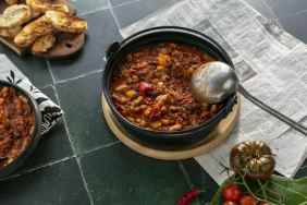 A bowl of chili with a ladle on some tile.