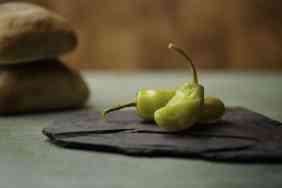 Two Pepperoncini Peppers on slate rock with wood background