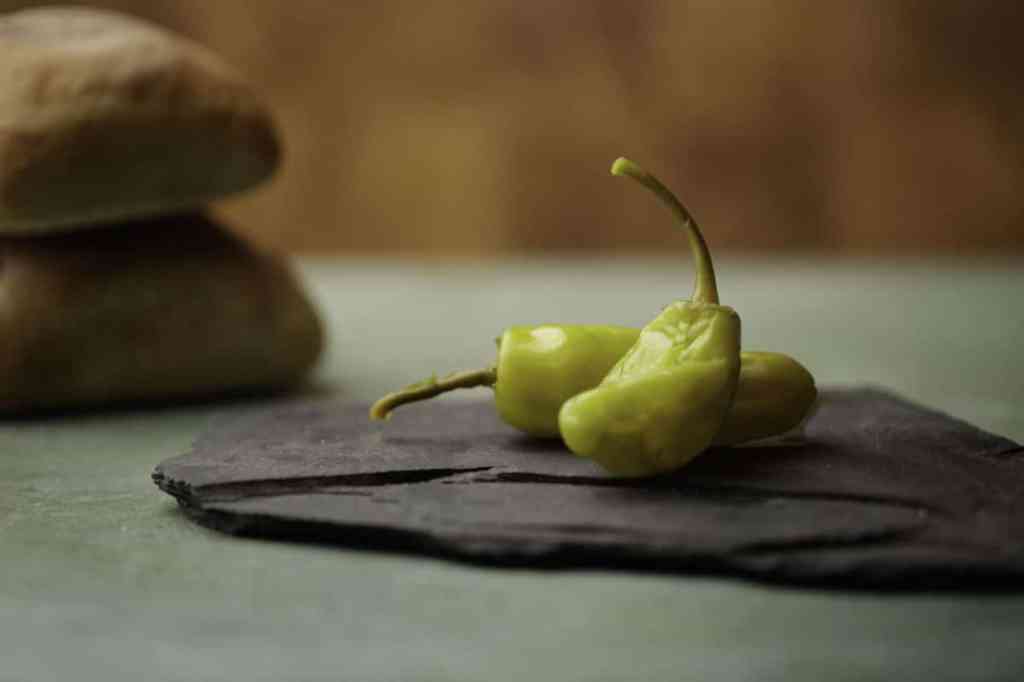 Two Pepperoncini Peppers on slate rock with wood background